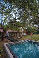 Una piscina rodeada de un jardín, con una casa al fondo.