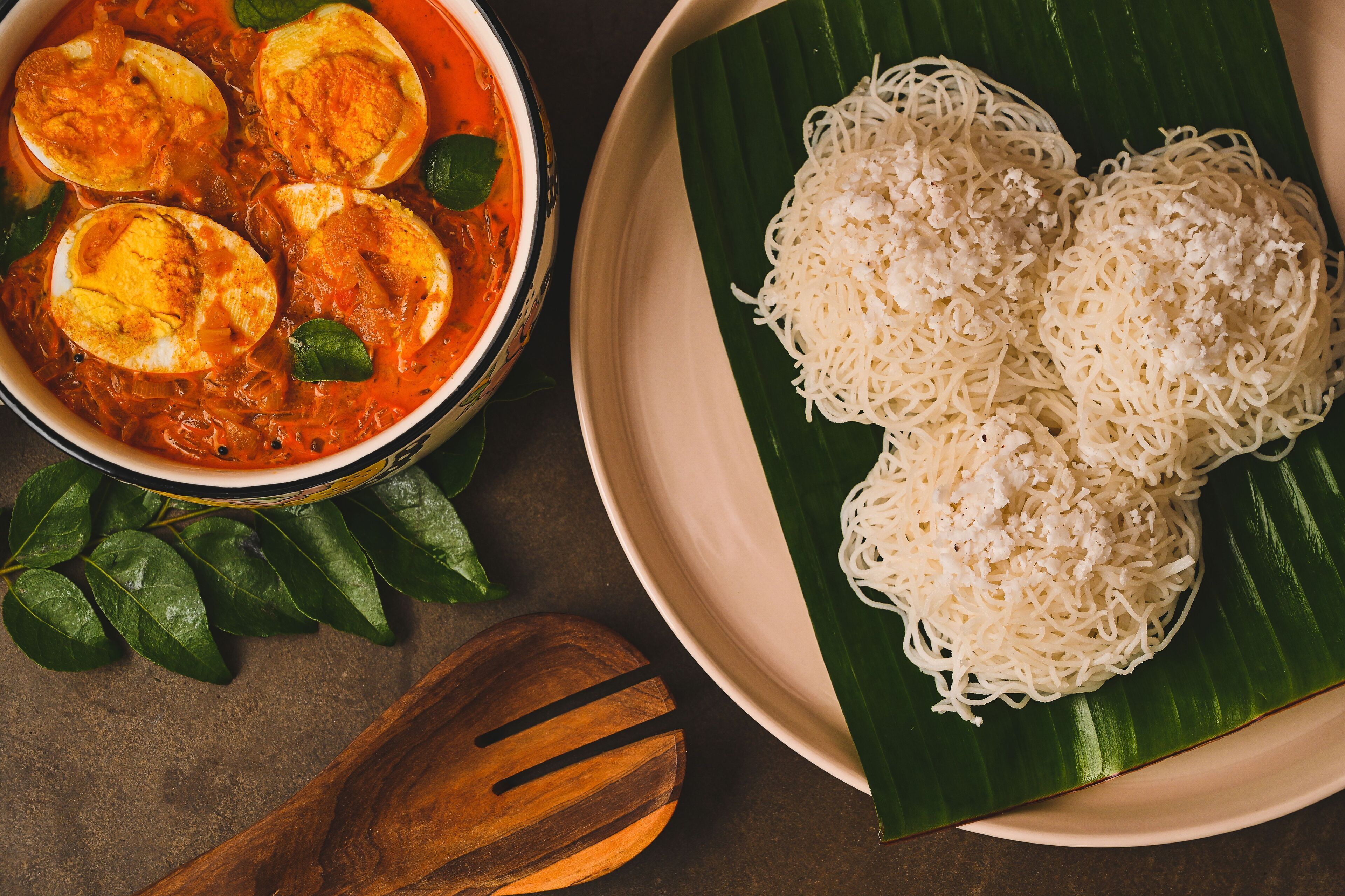 Un bol de curry aux œufs et une assiette de nouilles blanches, le tout servi sur une feuille de bananier.