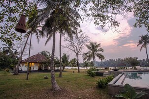A serene outdoor setting with a pool, palm trees, and a small building with a tiled roof.