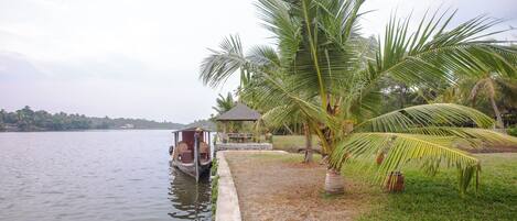 A calm lake with a boat docked on the left, a gazebo, and palm trees along the shore.