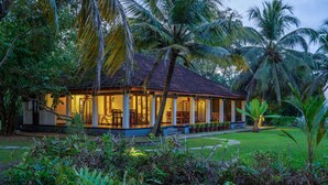Een huis met een overdekte veranda, omgeven door weelderige begroeiing en palmbomen.