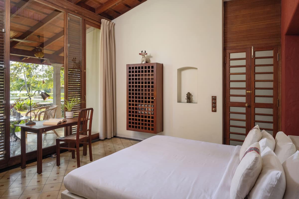 A hotel room with a bed, a wooden cabinet, a dining table with chairs, and a view of the outdoors.