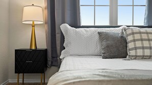Un dormitorio con cama, mesita de noche con lámpara y ventana con cortinas.