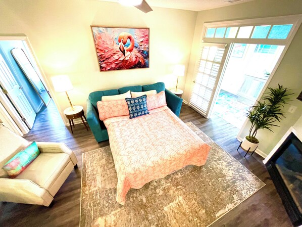 A spacious bedroom with a large bed, a teal sofa, a small side table, and a potted plant. - Cherry Moon -a charming 2-bedroom condo with WiFi, AC in welcoming Myrtle Beach (Myrtle Beach)