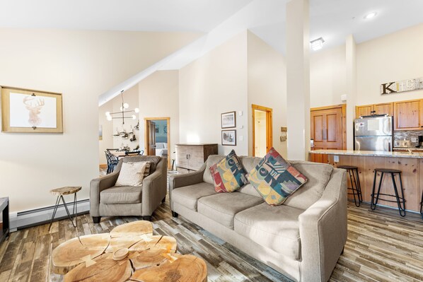A living room with a sofa, coffee table, and a kitchen area with wooden cabinets and a refrigerator. - Es8629-2 (Keystone)