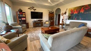 Un ampio soggiorno con una grande TV a schermo piatto, comodi posti a sedere e un quadro decorativo.