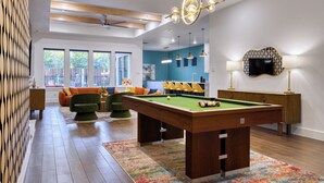 A modern living room with a pool table, comfortable seating, and a view of the outdoors.