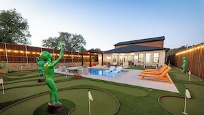 A backyard with a pool, artificial green grass, and a wooden fence.