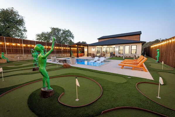 A backyard with a pool, artificial green grass, and a wooden fence.