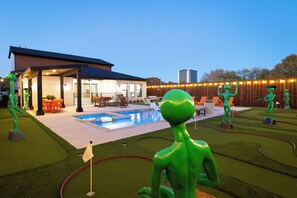 A backyard with a swimming pool, a covered patio, and decorative alien statues.