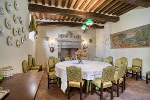 Une salle à manger avec une table ronde, des chaises recouvertes d’un tissu vert, une cheminée et un tableau au mur.
