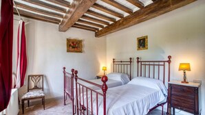 Une chambre avec deux lits, une chaise, une tête de lit en bois, une table de chevet et un radiateur.