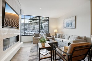 Un salon moderne doté d’une grande fenêtre, d’une cheminée et offrant une vue sur un paysage enneigé.