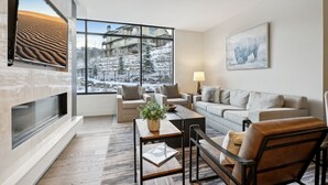 A modern living room with a large window, a fireplace, and a view of a snowy landscape. - Ski-In/Ski-Out Residence In The Heart Of Canyons Village (Park City)