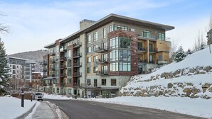A multi-story hotel with balconies, a snow-covered landscape, and a clear sky. - Ski-In/Ski-Out Residence In The Heart Of Canyons Village (Park City)