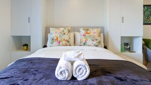 A neatly made bed with floral pillows, a pair of rolled towels, and a dark blue blanket. - Metro Escape Studio across South City Mall (Christchurch)