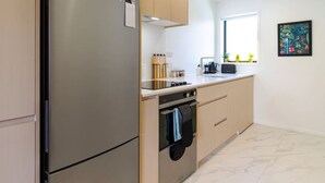 A modern kitchen with a stainless steel refrigerator, built-in oven, and a window with a view of plants. - Metro Escape Studio across South City Mall (Christchurch)