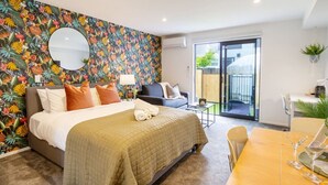 Ein Hotelzimmer mit Bett, Esstisch mit Stühlen, einem kleinen Balkon und einer Wand im tropischen Stil.