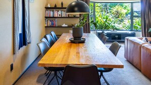 Een moderne eetruimte met een houten tafel, zwarte stoelen, een zwarte hanglamp, een boekenkast en een groot raam met uitzicht op groen.