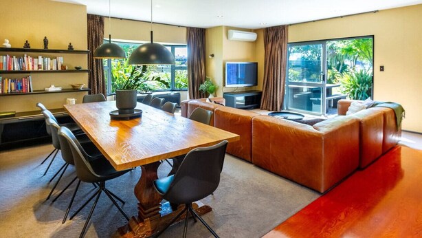 Een moderne woonkamer met een houten eettafel, zwarte stoelen, een leren bank en een televisie.