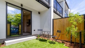 Une maison moderne avec une entrée dotée d’une porte en verre, un petit patio avec une table et des chaises, et une clôture en bois.