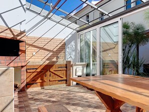 A patio area with a wooden table and a brick oven, a glass door leading to a room, and a view of a building with a red-tiled roof. - Eddys House by Atlantic Holiday (Água de Pena)