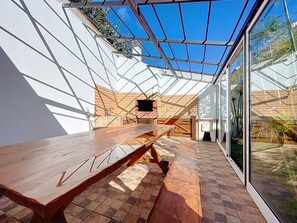 A sunlit patio with a wooden table, a brick wall, and a glass enclosure. - Eddys House by Atlantic Holiday (Água de Pena)