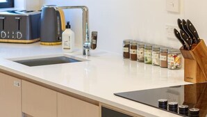 Eine moderne Küche mit weißer Arbeitsplatte, einem eingebauten Backofen, einer Kaffeemaschine und einem Messerblock.