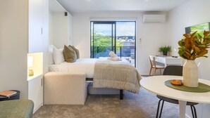 Ein modernes Schlafzimmer mit Bett, Schreibtisch, Stuhl und Blick ins Grüne.