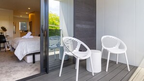 Ein modernes Schlafzimmer mit einem großen Bett, einer Glastür, die auf einen Balkon führt, und einem kleinen Tisch mit zwei weißen Stühlen.