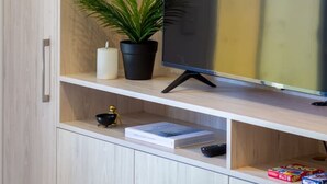 Un mueble de entretenimiento moderno con un televisor de pantalla plana, una planta en maceta y un estante pequeño con un libro y un control remoto.
