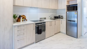 Una cocina moderna con armarios de madera clara, electrodomésticos de acero inoxidable y piso de mármol.