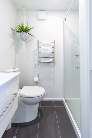 Une salle de bain moderne équipée de toilettes, d’un porte-serviettes, d’une plante suspendue et d’une cabine de douche en verre.
