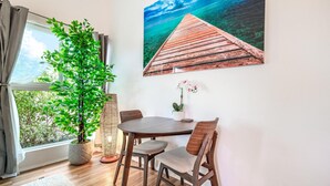 Ein Essbereich mit Holztisch und -stühlen, einem Blumentopf, einem Gemälde eines hölzernen Piers und Blick durch ein Fenster.