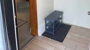 A room with a wooden door, a small table, a shelf with hanging items, and a carpeted floor.