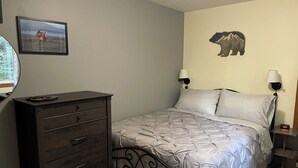 A bedroom with a bed, a dresser, a wall-mounted lamp, a clock, and a framed picture.