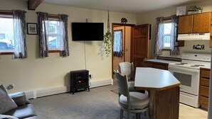 A compact kitchen with a stove, a dining table with chairs, a TV mounted on the wall, and a heater.
