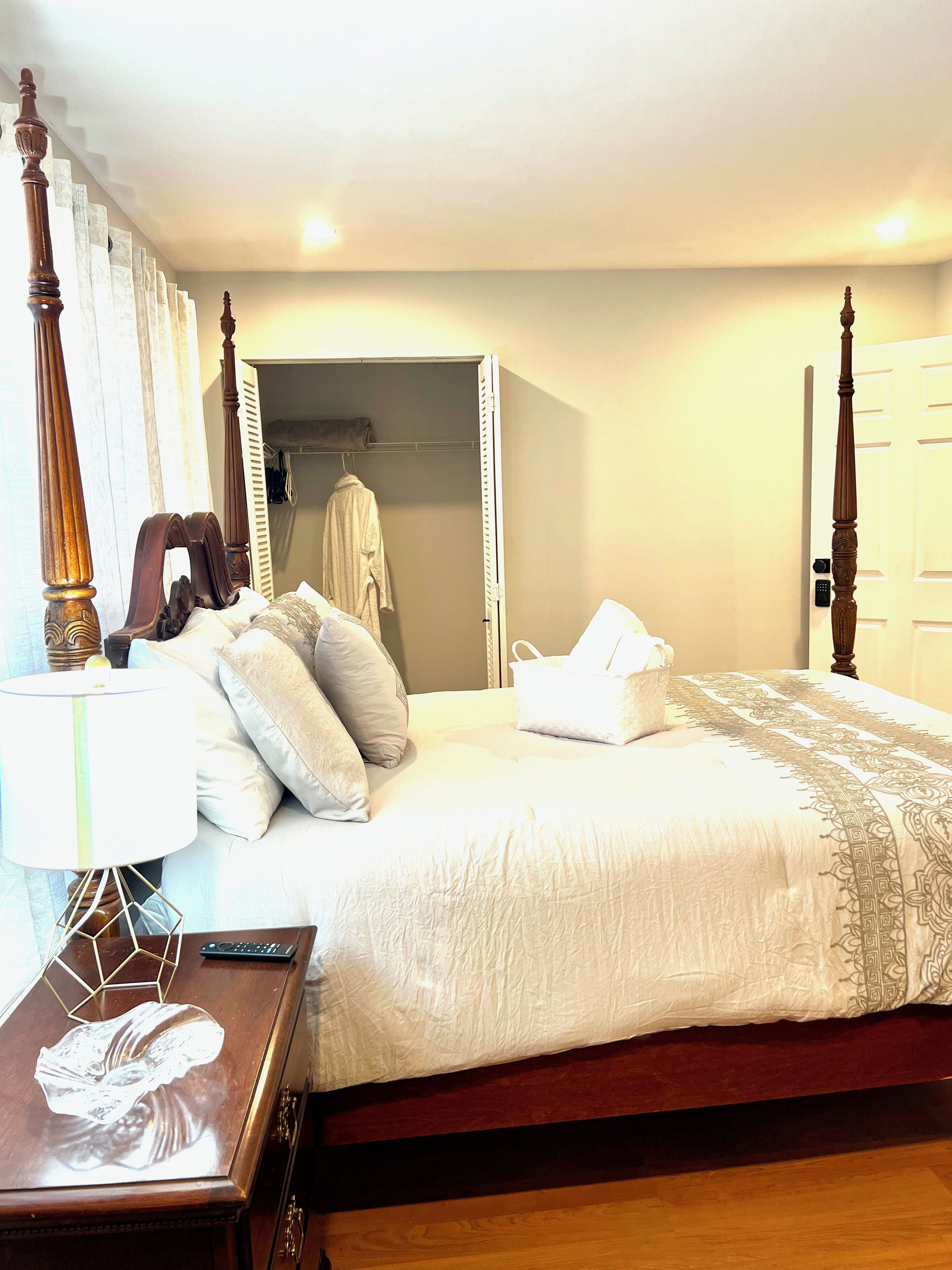 A neatly made bed with a white comforter and pillows, a wooden nightstand with a lamp, and a wooden floor.