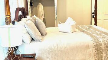 A neatly made bed with a white comforter and pillows, a wooden nightstand with a lamp, and a wooden floor.