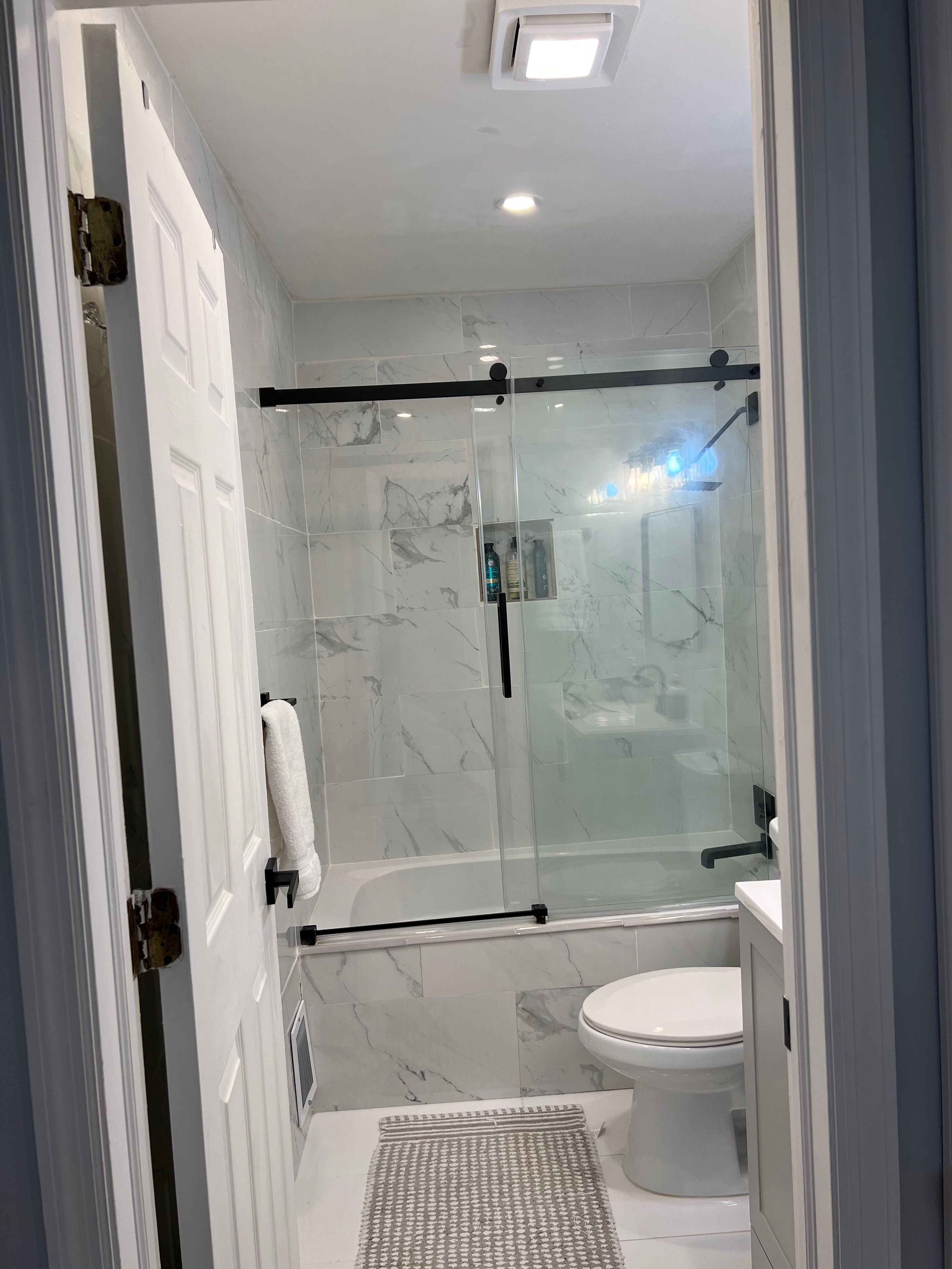 A modern bathroom with a glass-enclosed shower, a white toilet, and a marble-tiled floor.