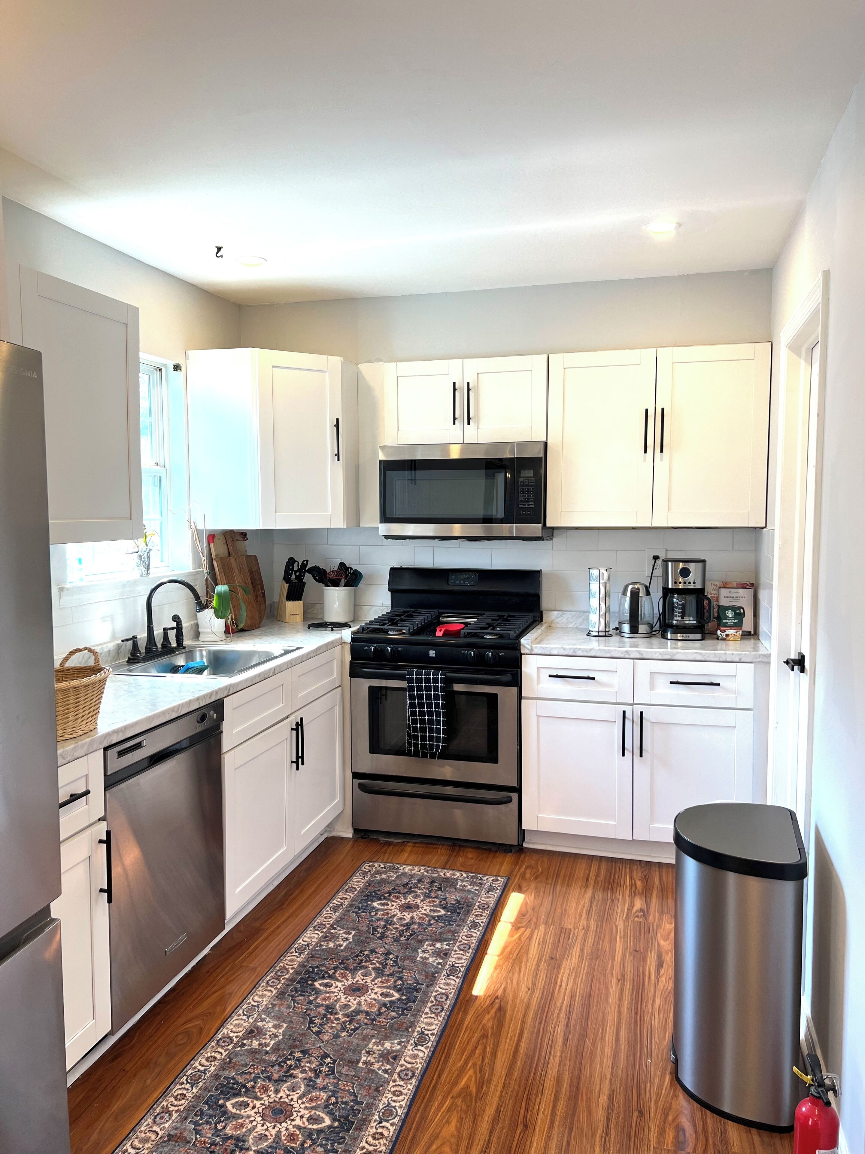 A modern kitchen with white cabinets, stainless steel appliances, and a wooden floor.