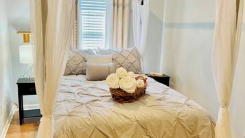 Quarto com cama de dossel, mesa de cabeceira, luminária e janela com cortinas.