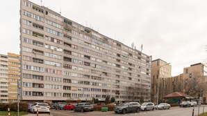Un edificio residencial de varios pisos con fachada uniforme, varios balcones y un estacionamiento con distintos automóviles.