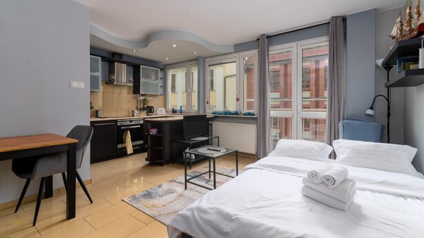 Una habitación de hotel moderna con cama, escritorio, kitchenette y ventanas amplias.