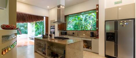 A modern kitchen with a central island, stainless steel appliances, and a large window with a tropical view.