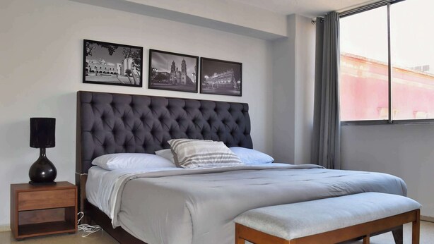 A bedroom with a large bed, a bedside table, a bench, and three framed pictures on the wall. - depa 205 · Department in the Historic Center 205 (San Luis Potosí)