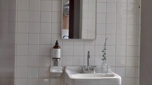 A bathroom with a white tiled wall, a mirror, a sink, a soap dispenser, and a glass jar with a plant. - depa 205 · Department in the Historic Center 205 (San Luis Potosí)