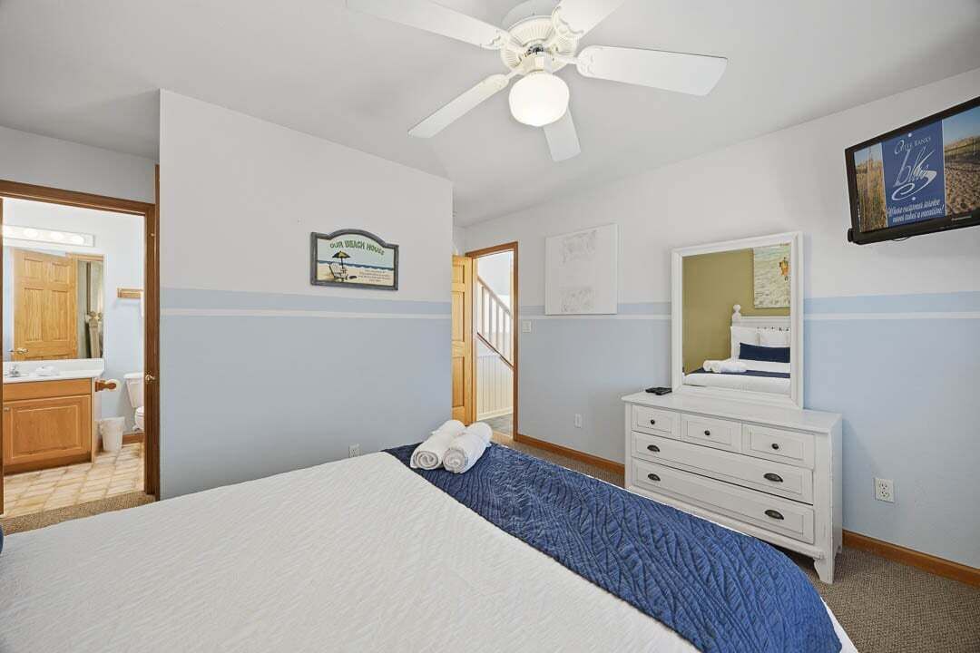A bedroom with a bed, a dresser, a ceiling fan, and a framed picture on the wall.