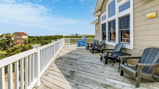 Une terrasse en bois avec des chaises, dont une chaise Adirondack bleue, donnant sur un quartier résidentiel.