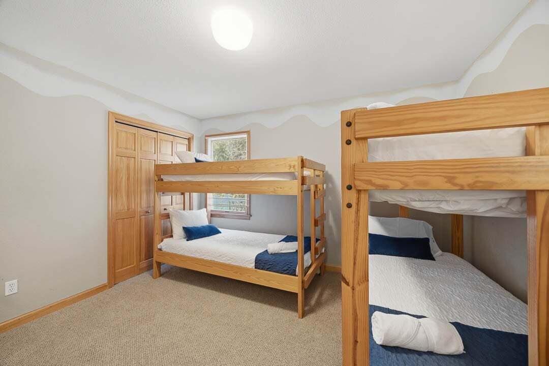 A room with two bunk beds, a wooden wardrobe, a window, and a ceiling light.